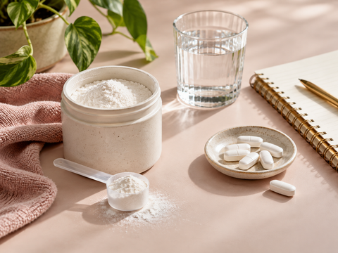 Unbranded wellness powder and tablets beside water and a notebook